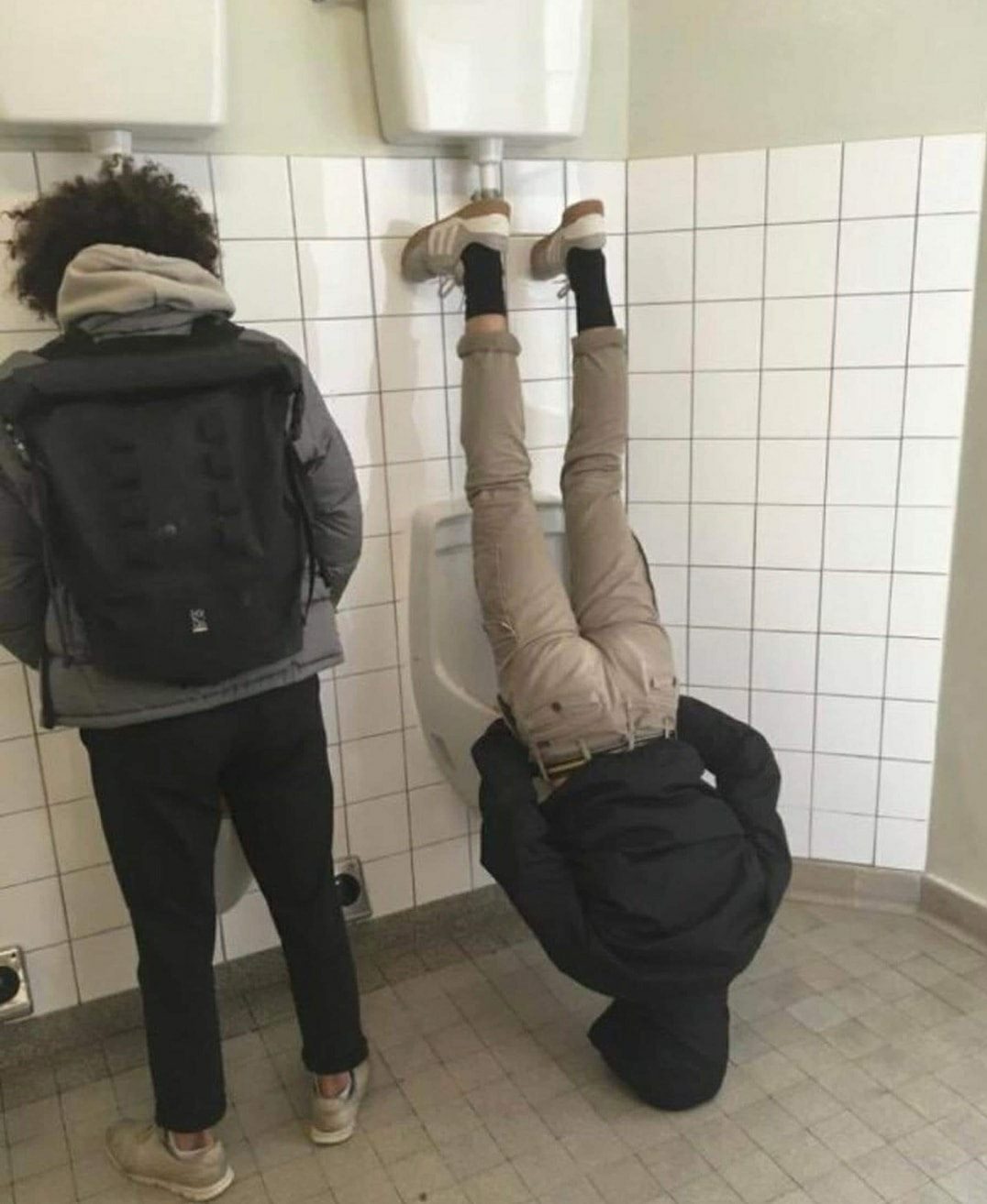 This meme features a person in a bathroom stall, with their pants down and their legs up on the toilet, but instead of using the toilet, they're urinating on the wall. The text "I can pee standing up" is often seen above the urinal, but in this image, it's been modified to "I can pee standing up, but I'll pee on the wall instead".